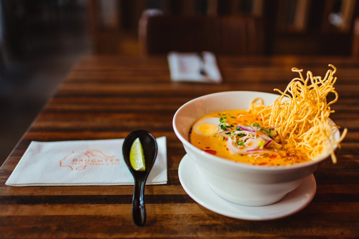 a bowl of soup with noodles and a spoon on a table at Daughter Thai Kitchen & Bar