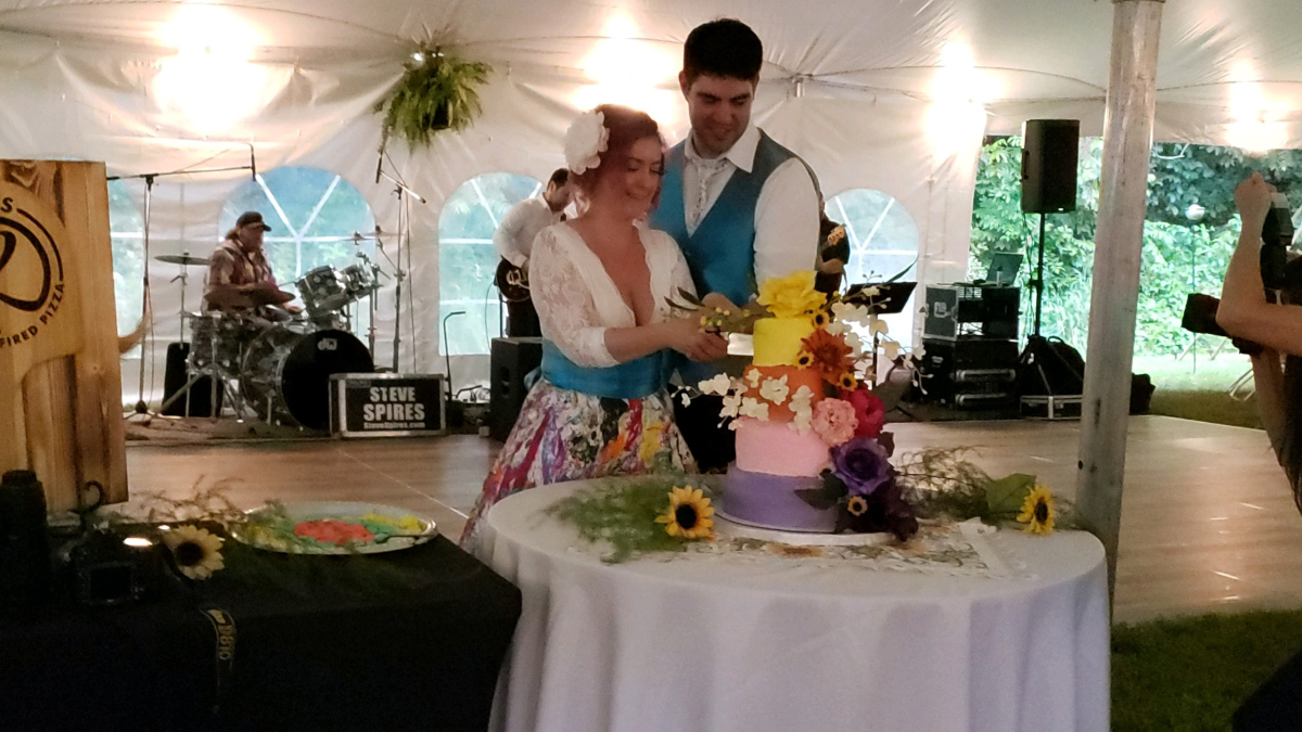A bride and groom stand together cutting a colorful tiered wedding cake