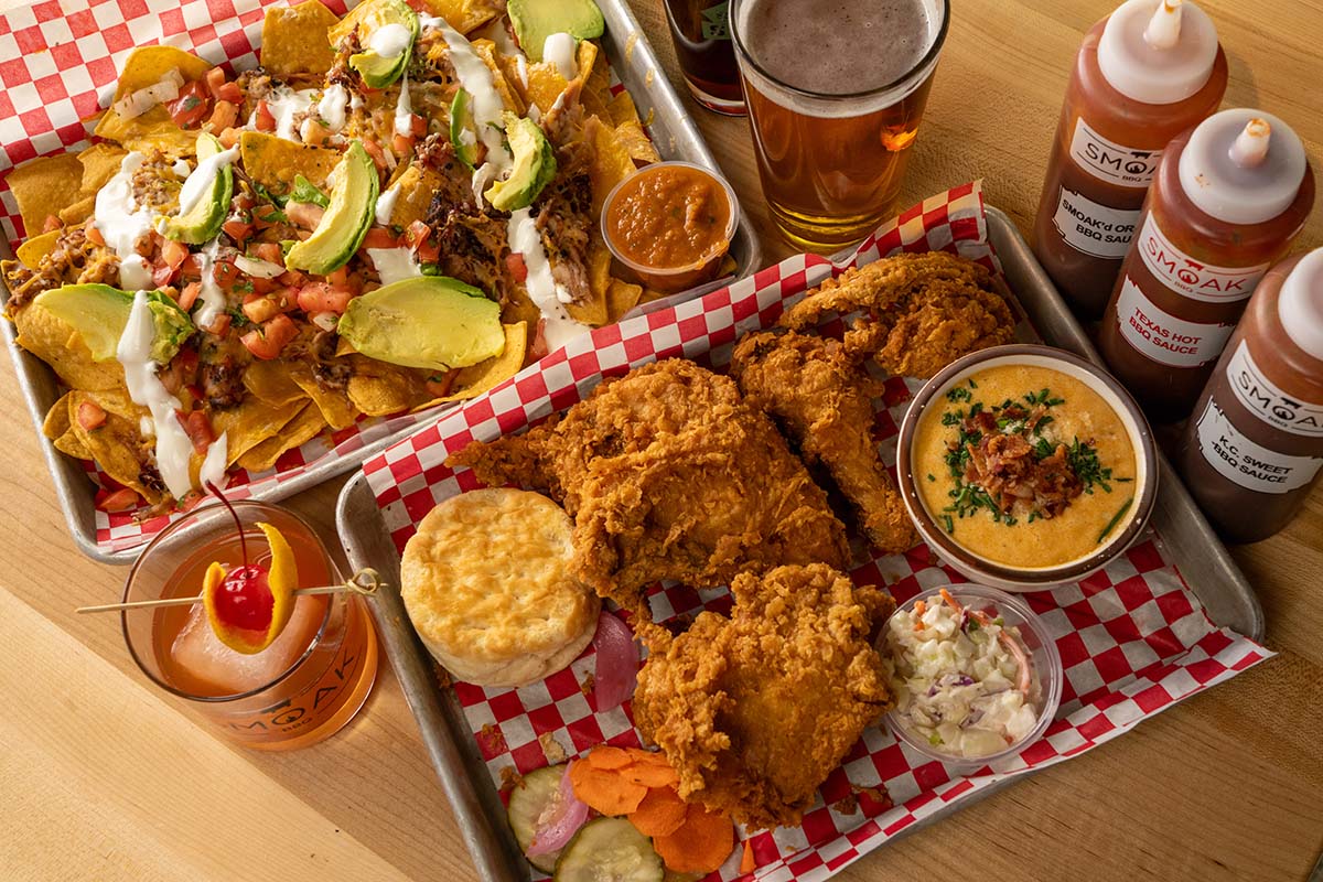 Trays of loaded nachos and fried chicken with beverages and sauces