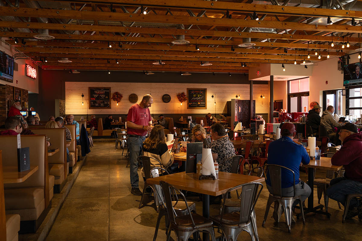 Interior of a busy restaurant with wooden tables, metal chairs, and fall decorations
