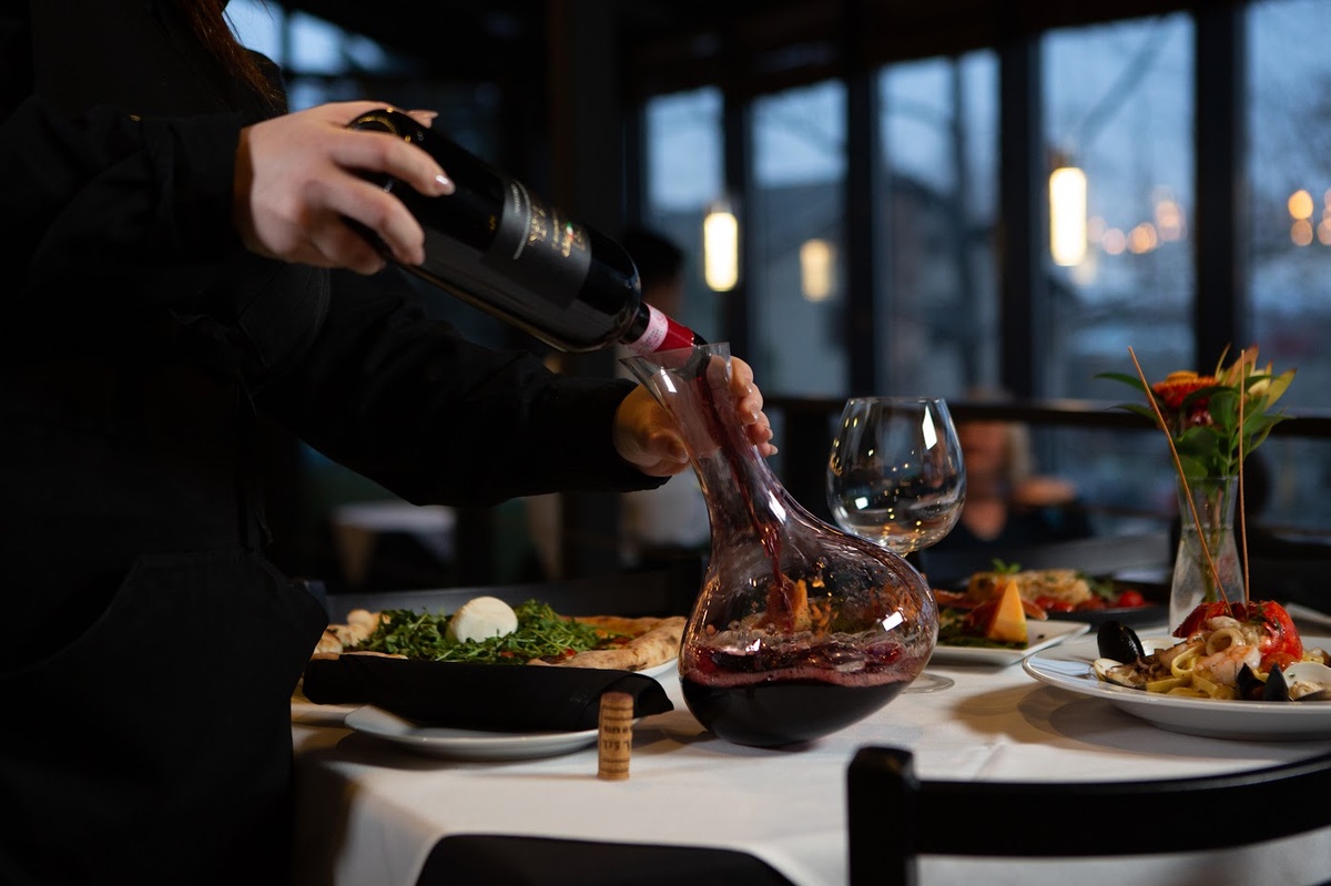 Server decanting red wine at a table with served food