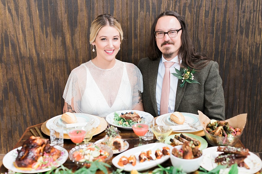 a bride and groom are posing for a photo in front of a table full of food.