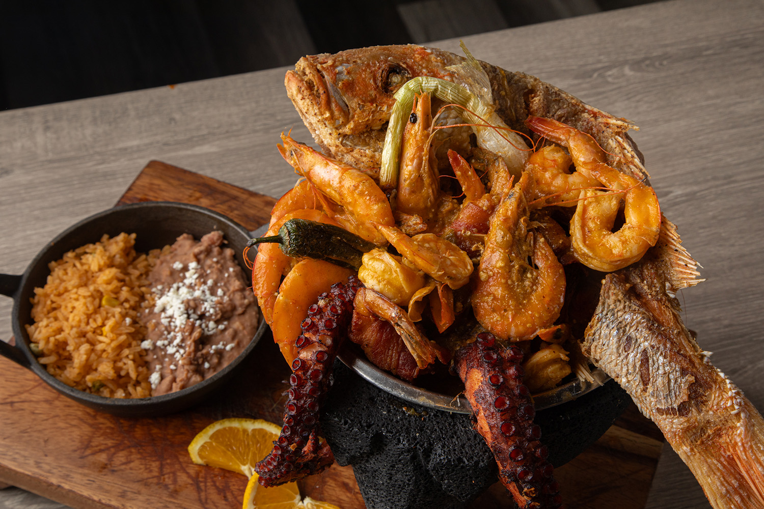 A seafood platter with a whole red fish, shrimp, prawns, and octopus on a wooden board
