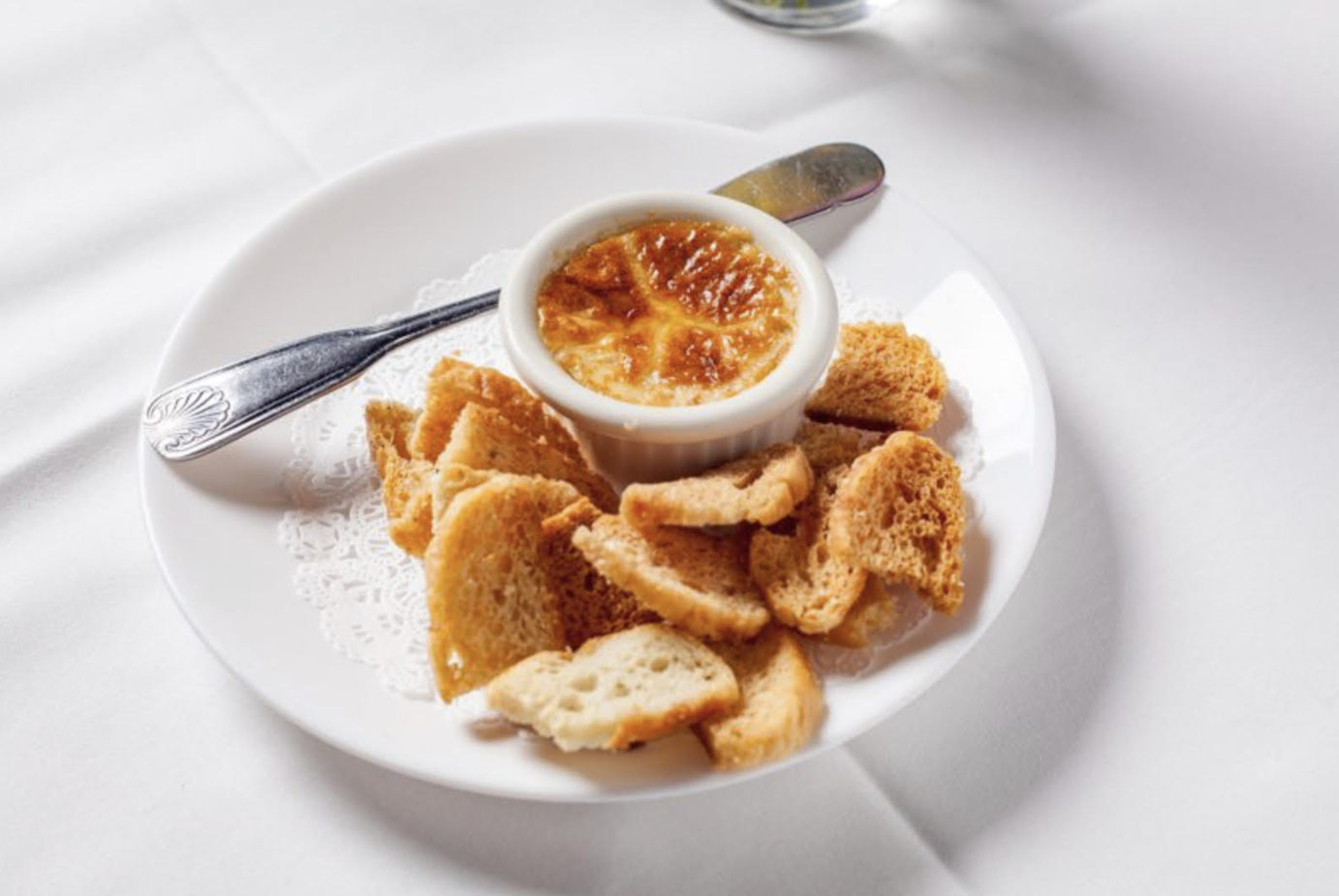 A ramekin of crème brûlée served with crispy bread slices on a white plate