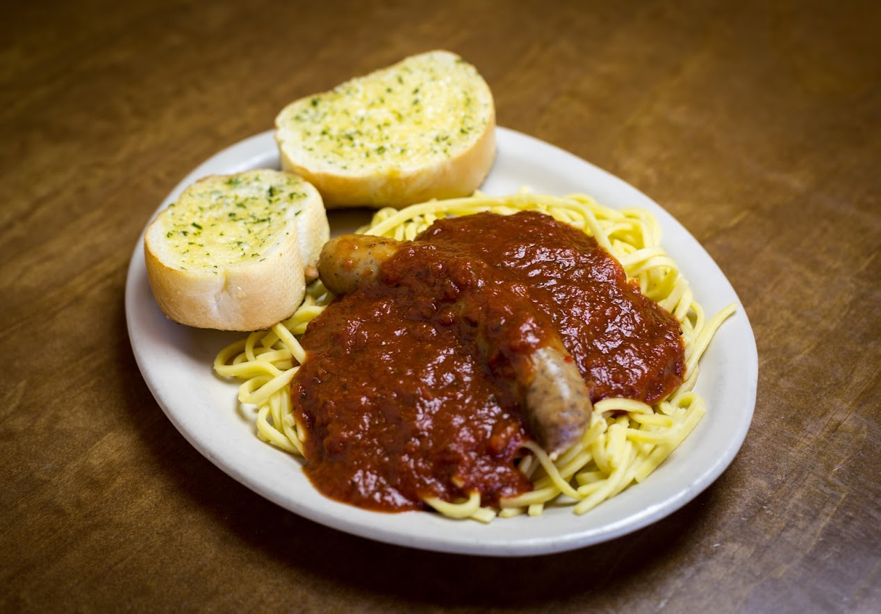 Spaghetti topped with sausage and sauce, served with garlic bread