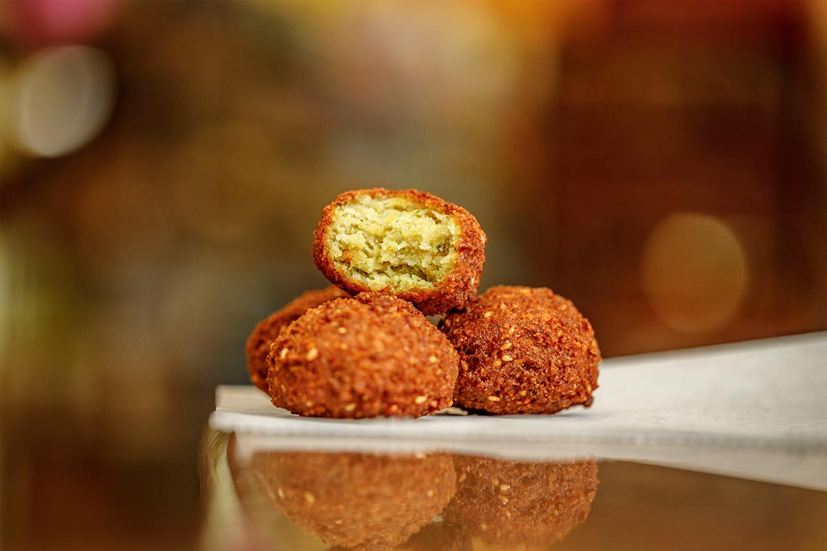 Golden fried falafel balls stacked on white plate, one cut open