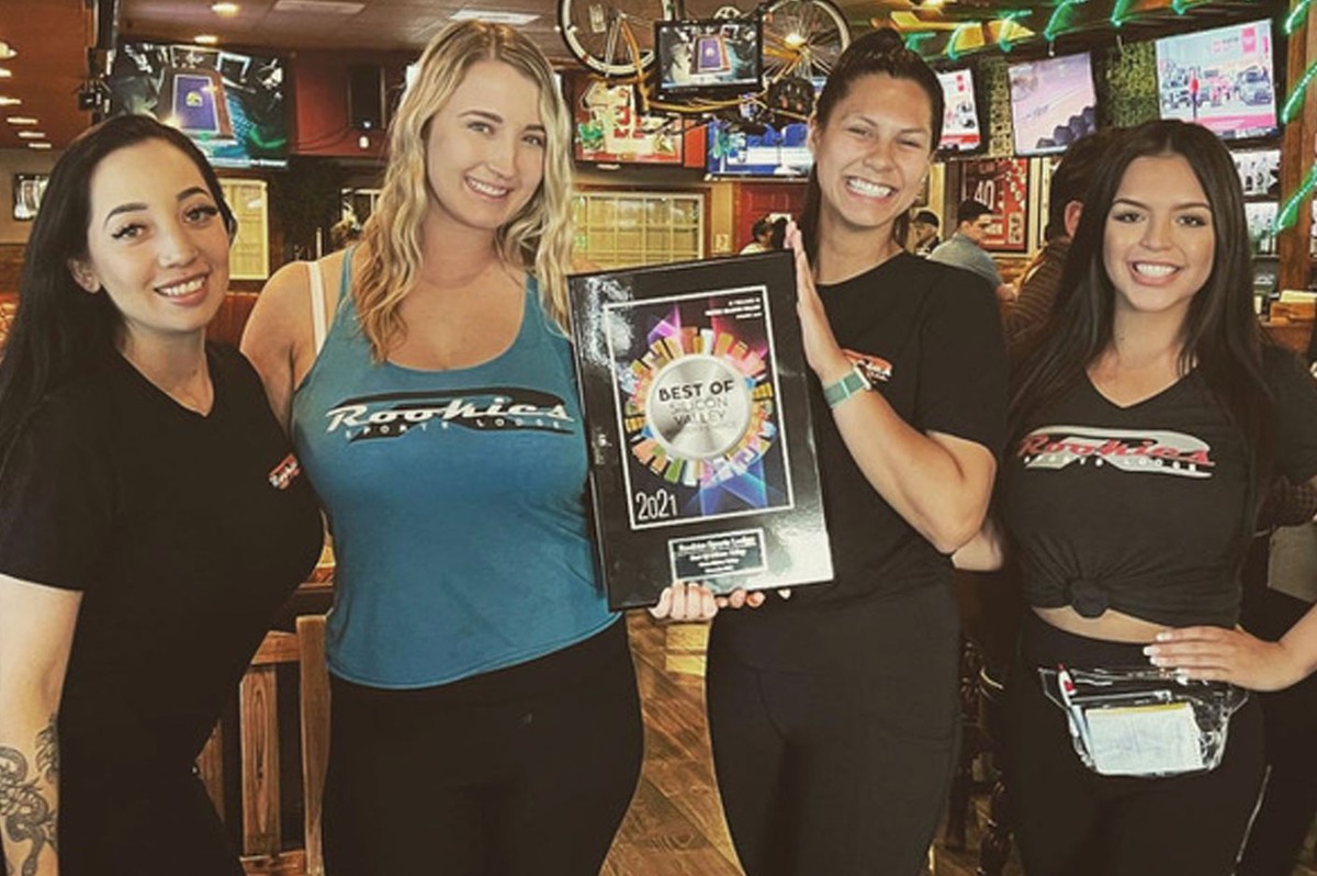 Four women posing with a plaque in front of a bar