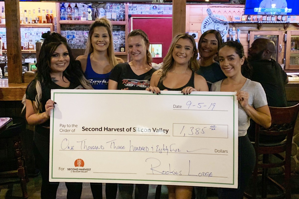 A group of women holding a check in front of a bar