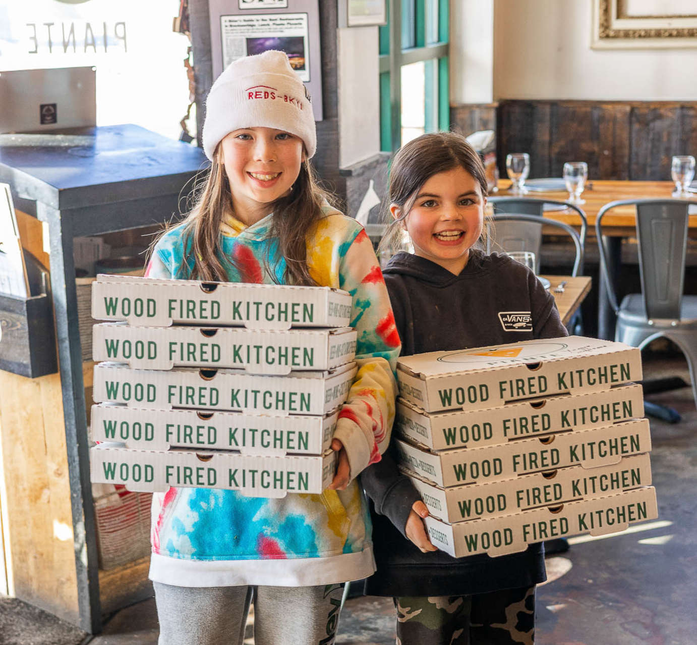 Two girls holding five pizza boxes each