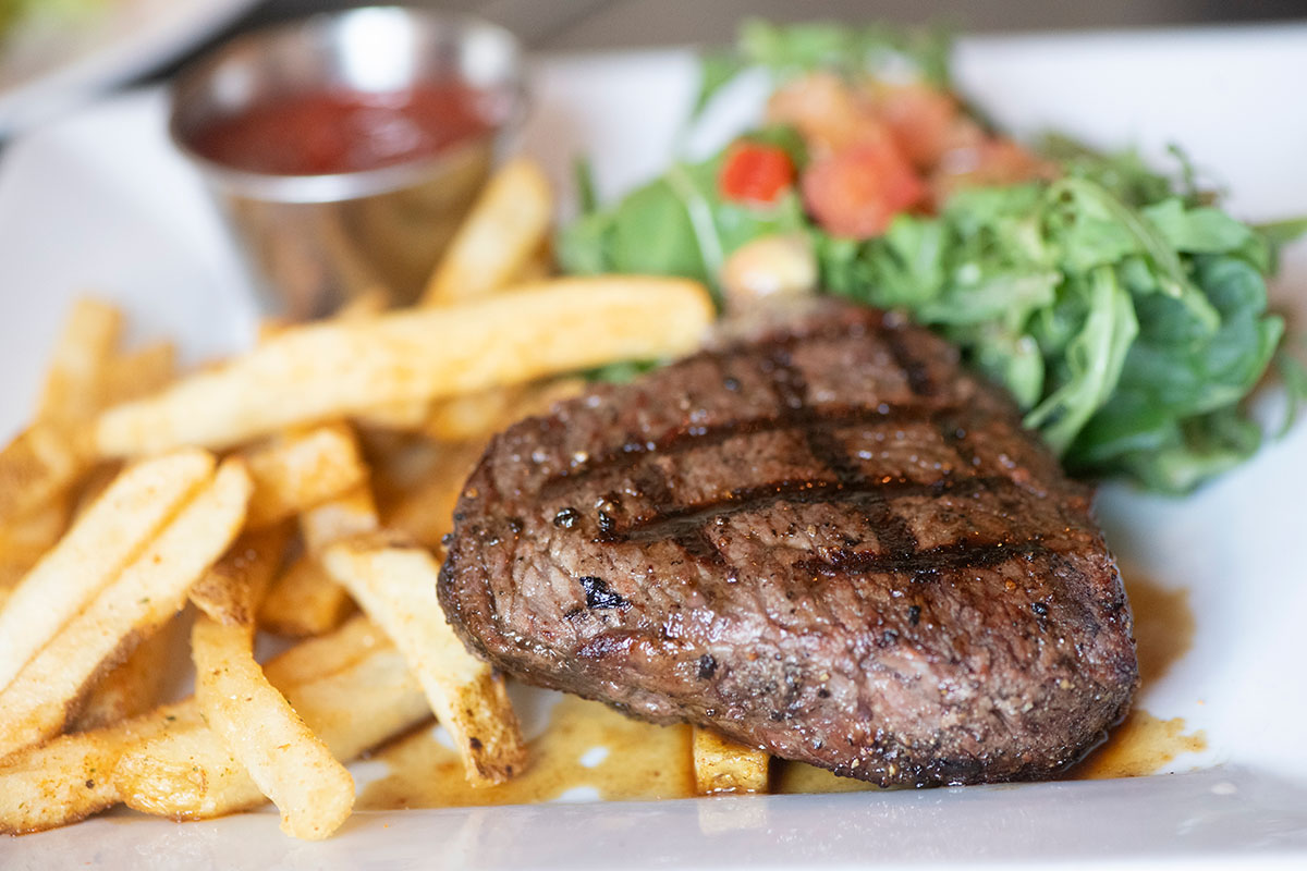 Close-up of a grilled steak with French fries, salad, and ketchup