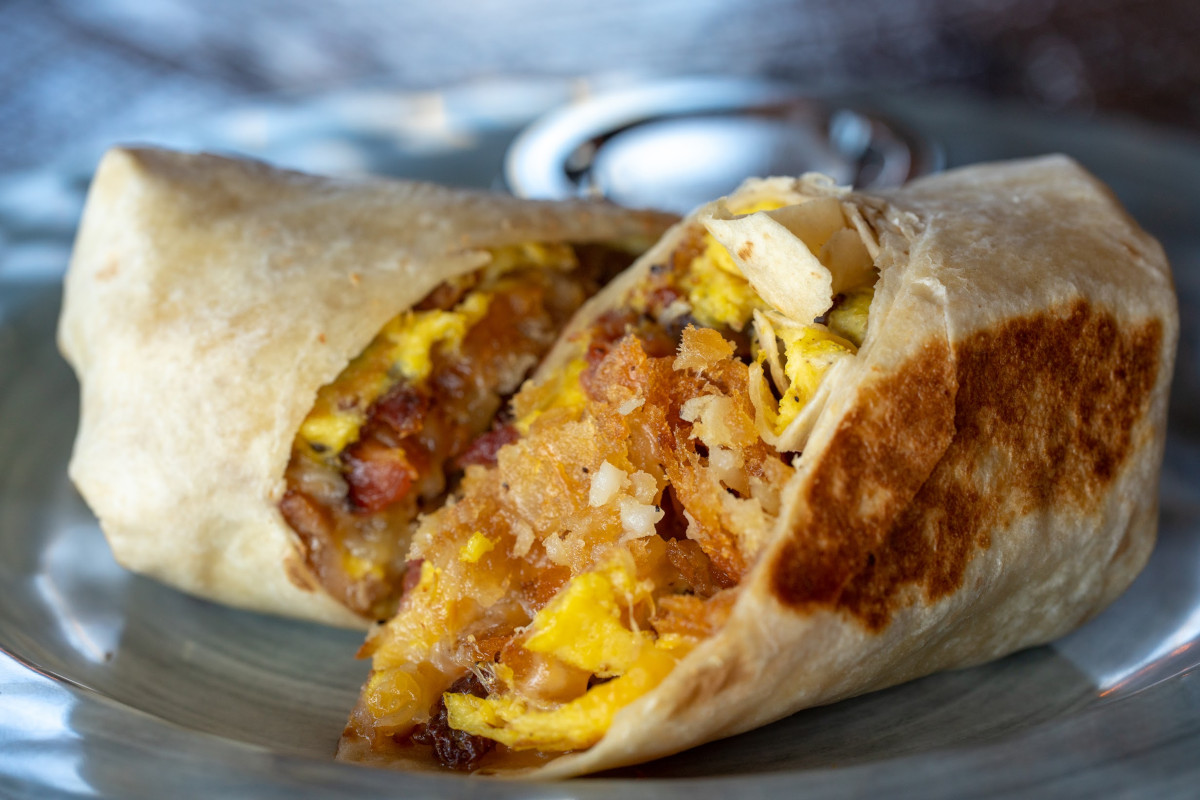 A burrito with eggs and bacon on a plate.