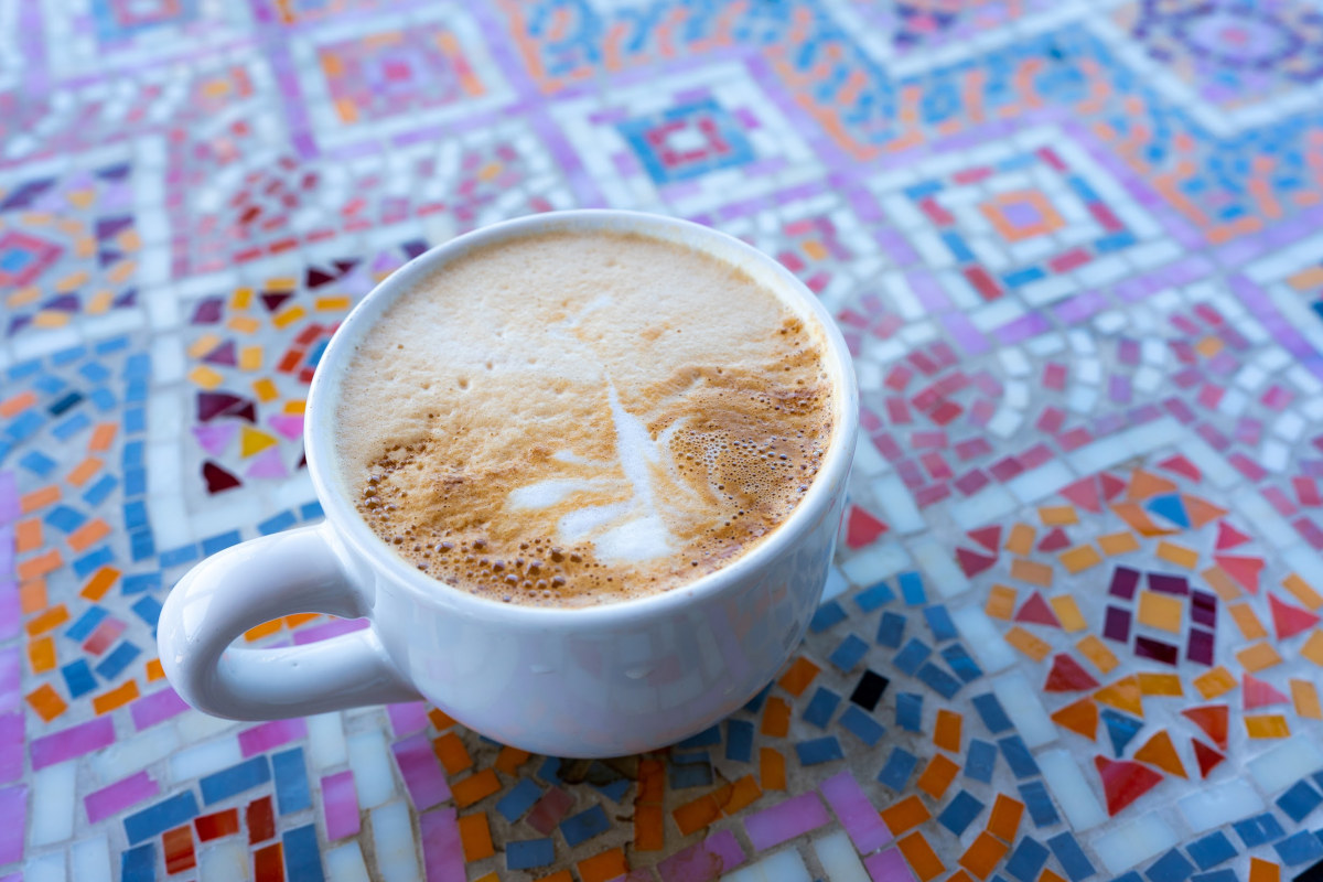 A cup of coffee sits on a colorful tiled table.