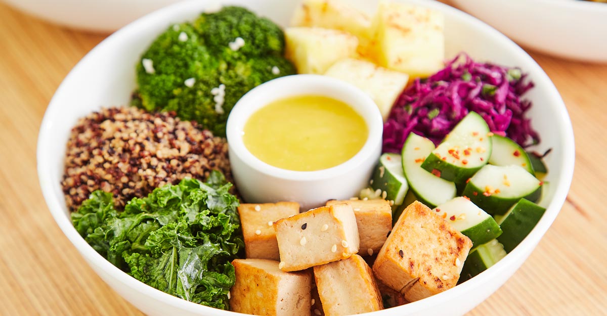 Salad of quinoa, greens, veggies and Asian tofu, served in a bowl with dressing dip
