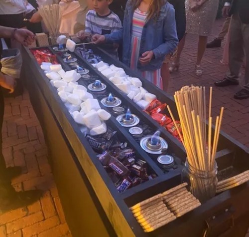 a group of people standing around a table with marshmallows and sticks