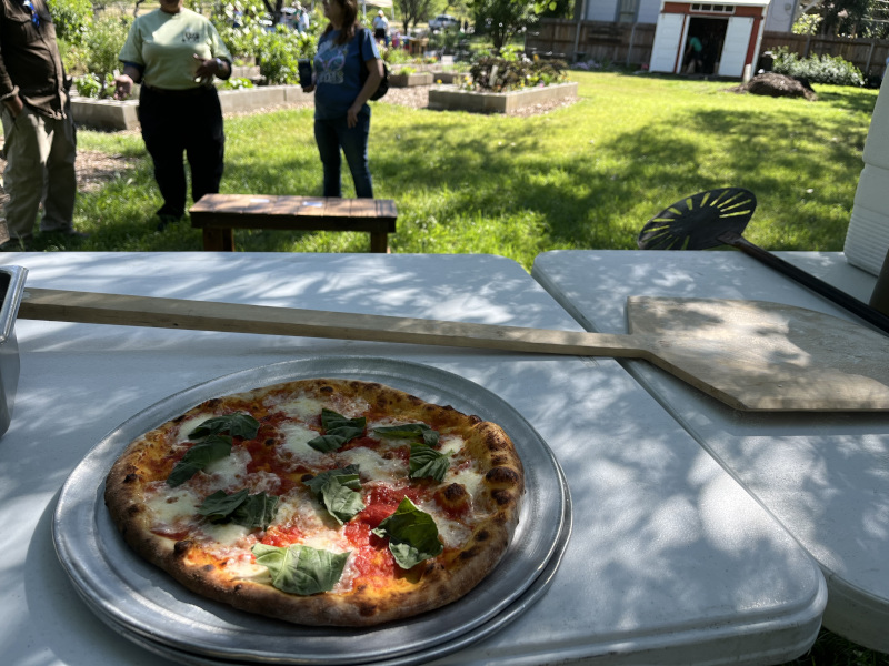 Margherita pizza on a table with two people in the background at an outdoor setting.