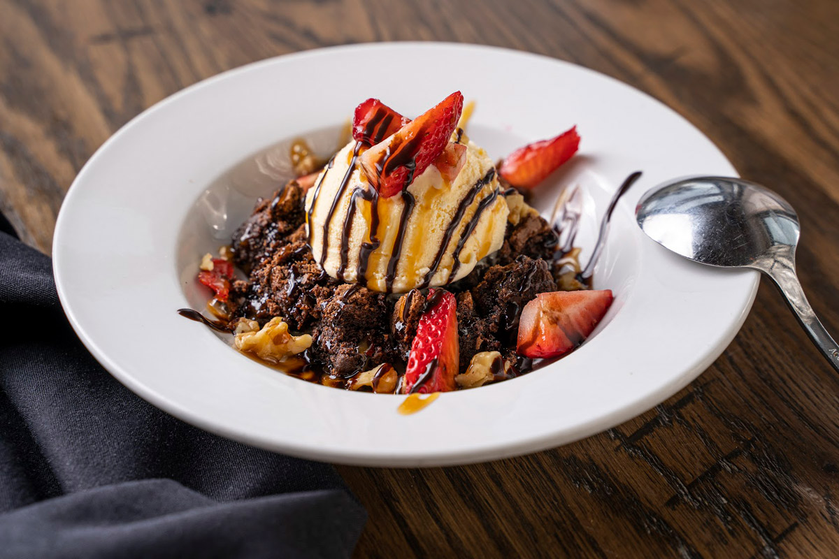 Brownie topped with ice cream, strawberry, and nuts